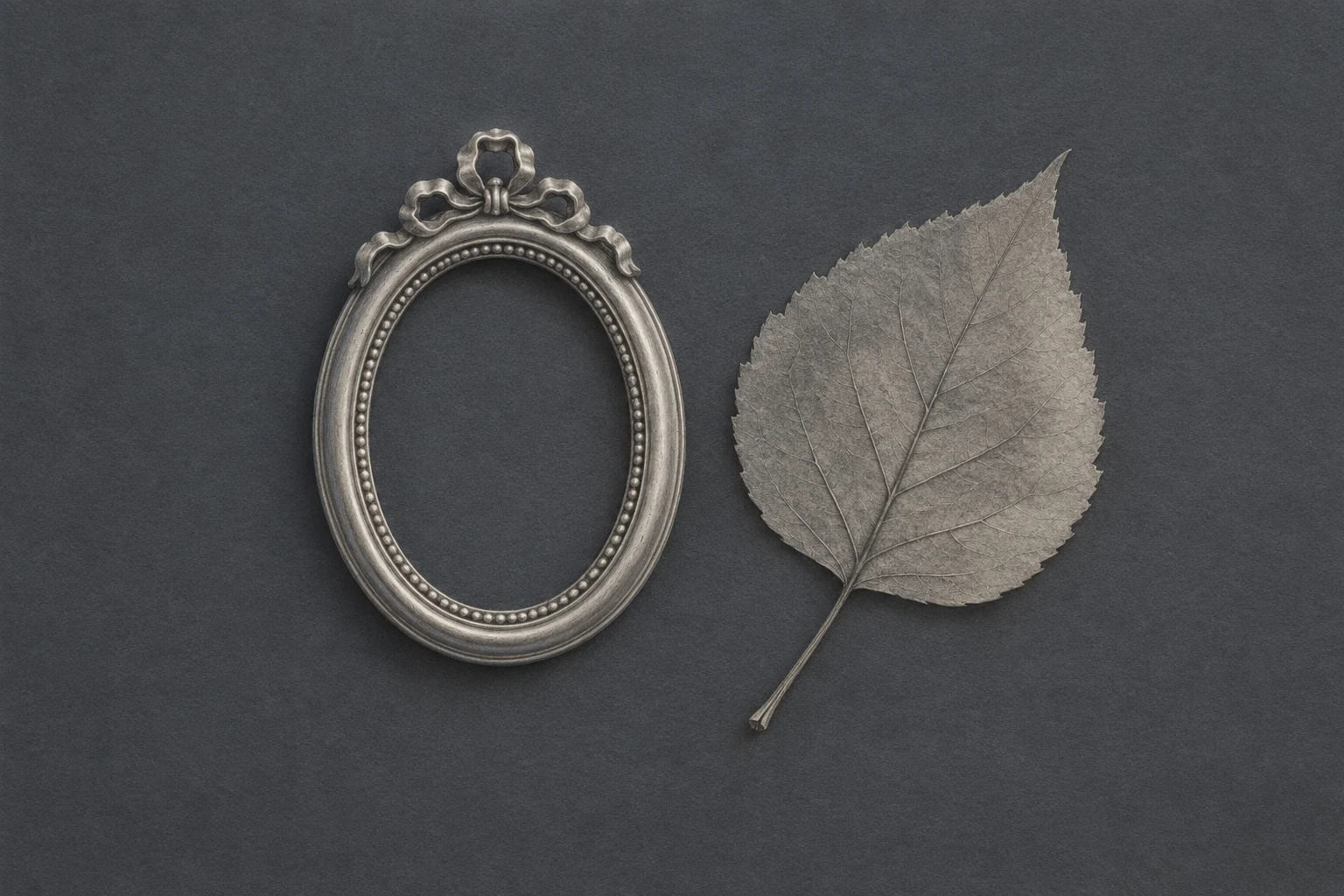 A graphite keepsake frame beside one pressed leaf.