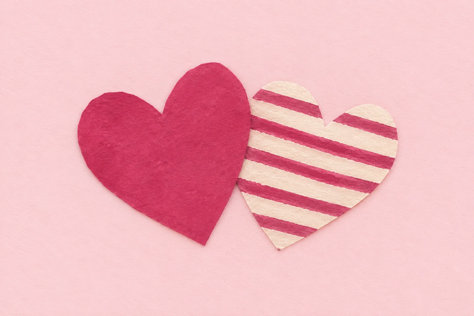 Two raspberry paper hearts leaning together.